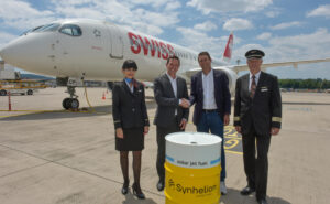 SWISS crew standing in front of an aircraft and a Synhelion barrel.
