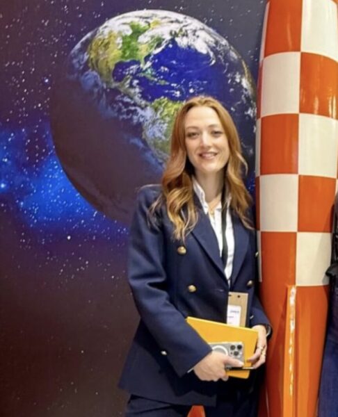 Laura Rösges is pictured standing in front of a photo of earth, and beside an orange and white rocket
