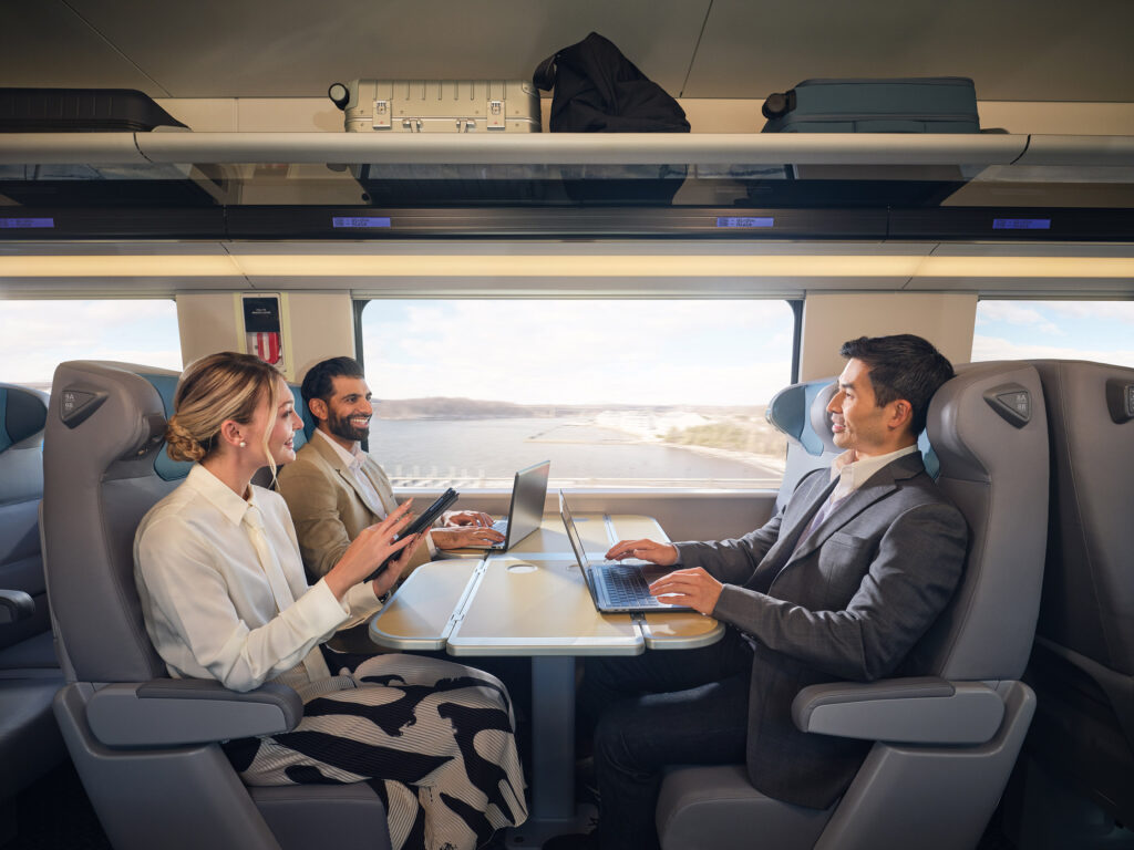 Passengers are using various devices in a four-seat arrangement with a table
