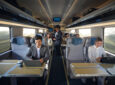 Inside the NextGen Acela rail car passengers are doing various activities at their seats, such as working on laptops, looking at their mobile devices and socializing.