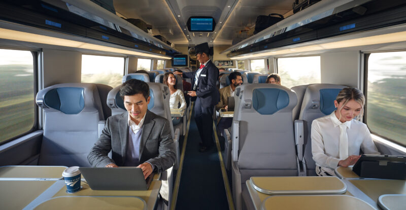Inside the NextGen Acela rail car passengers are doing various activities at their seats, such as working on laptops, looking at their mobile devices and socializing.
