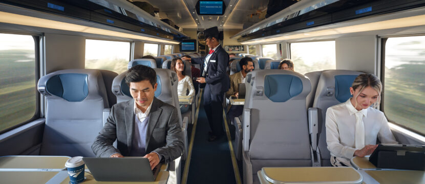 Inside the NextGen Acela rail car passengers are doing various activities at their seats, such as working on laptops, looking at their mobile devices and socializing.