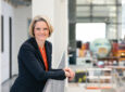Nicole Dreyer-Langlet smiling towards the camera whilst an aircraft is being assembled behind her.