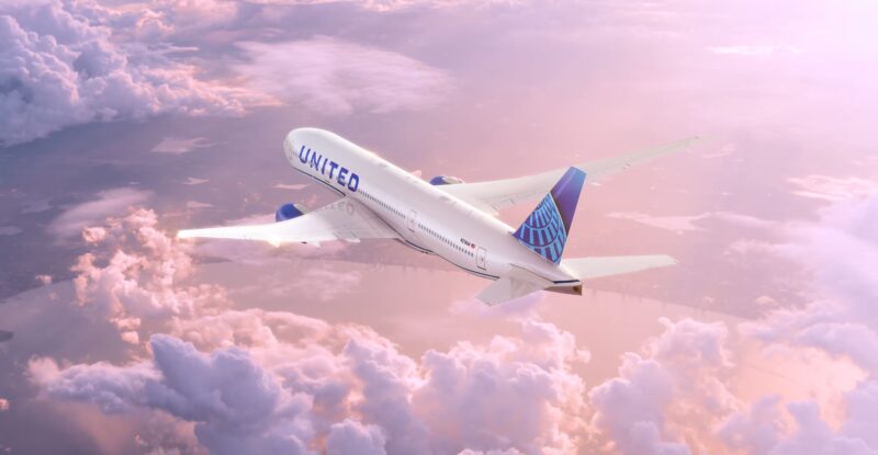 United Airlines Boeing 777 inflight above pink clouds.