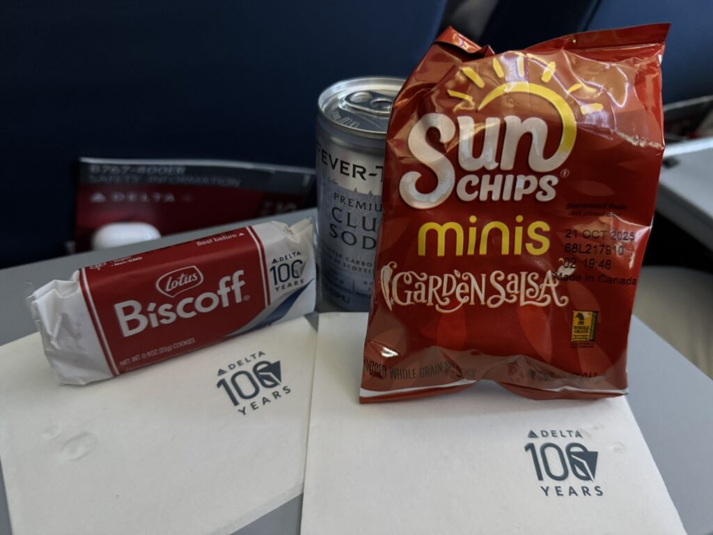 A bag of Sun Chips and Biscoff cookies sit on the aircraft tray table. 