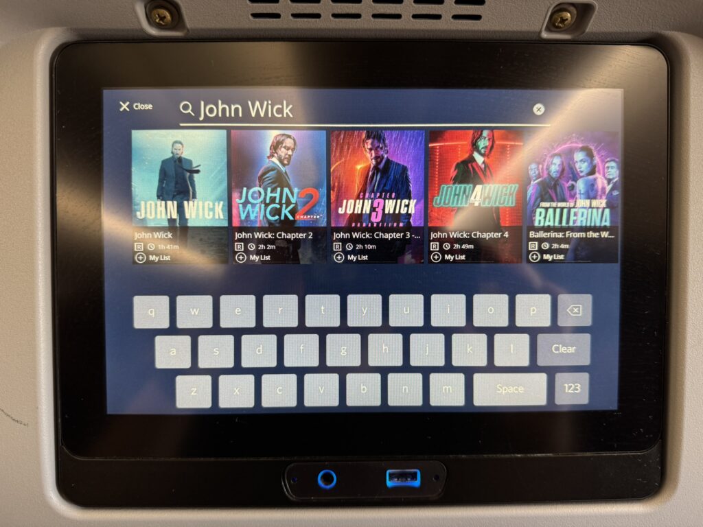 The seatback IFE is showing various movie options.