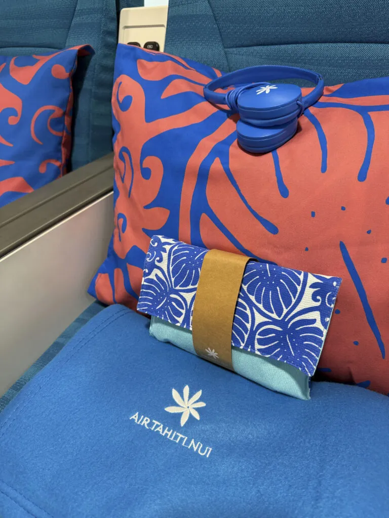 Large pillow, blanket and amenity kit sit on top of the seat with blue headphones