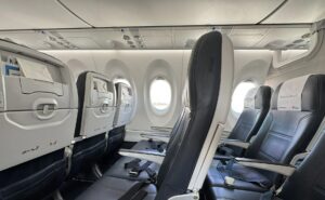 Smartwings Airbus A220-300 cabin with seats, PSUs and the bottom part of the current pivot bins in view.
