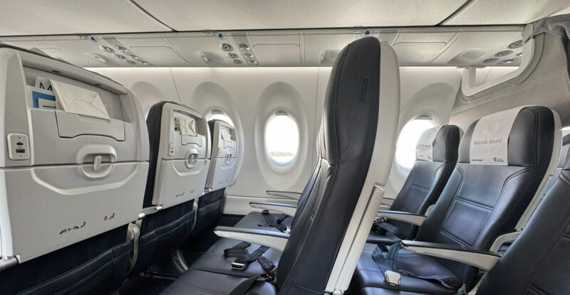 Smartwings Airbus A220-300 cabin with seats, PSUs and the bottom part of the current pivot bins in view.