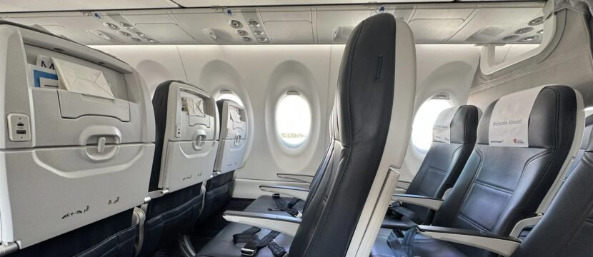 Smartwings Airbus A220-300 cabin with seats, PSUs and the bottom part of the current pivot bins in view.