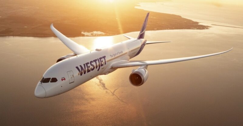 WestJet 787 aircraft inflight over a body of water at sunset.