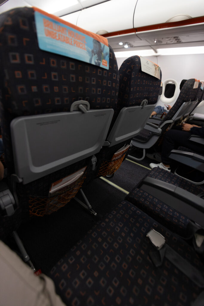The seatback shows a tray table stowed away and the close proximity of the seats.