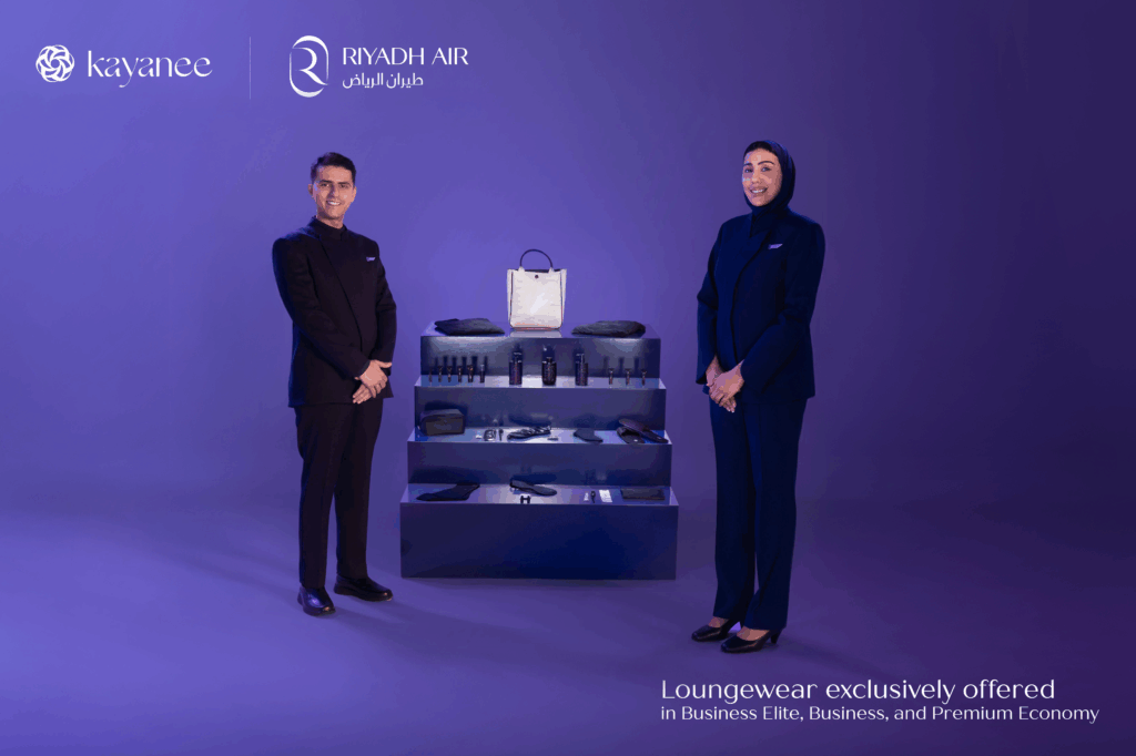 Two Riyadh Air crew members stand next to the amenity kit on display.