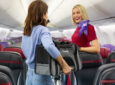 A passenger is holding a pet carrier while speaking with a Virgin Australia crew member in the aircraft cabin.