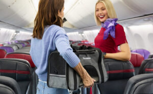 A passenger is holding a pet carrier while speaking with a Virgin Australia crew member in the aircraft cabin.