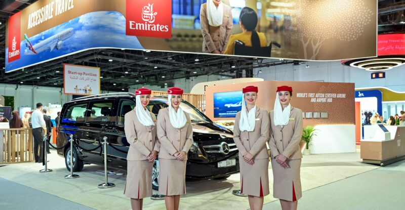 Emirates' stand at the 7th edition of AccessAbilities Expo in Dubai World Trade Centre with 4 flight crew members in uniform standing in front of it.