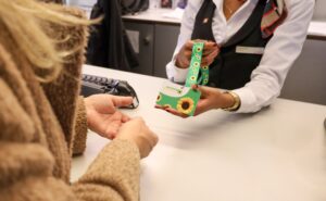 A SWISS crew member is handing a sunflower lanyard to a passenger.