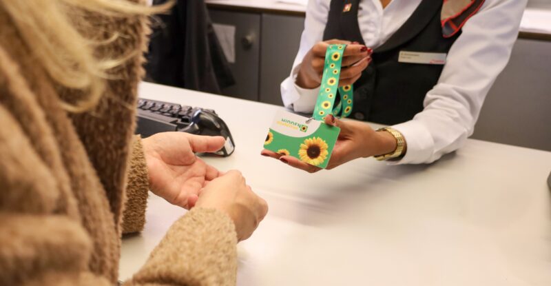 A SWISS crew member is handing a sunflower lanyard to a passenger.