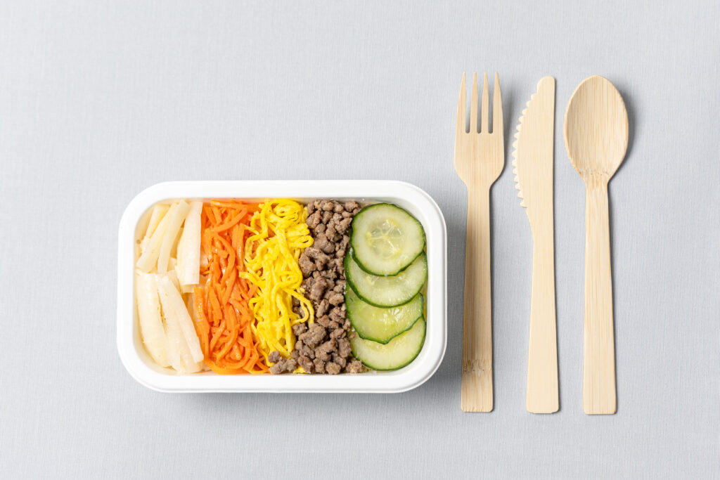 Korean Air meal in a plant-based container next to bamboo utensils.