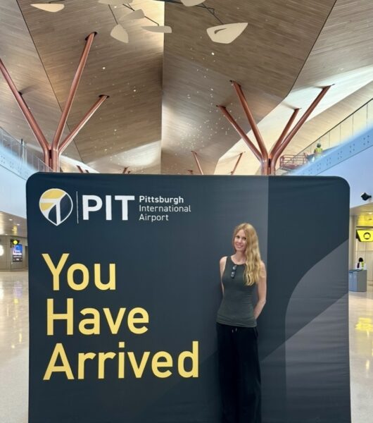Mary Kirby in front of a sign saying, "PIT, you have arrived."