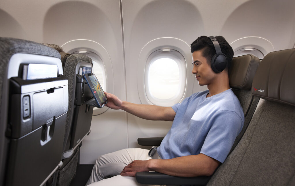 Male passenger enjoys watching his device in the seatback device holder whilst seating in an extra-legroom Qantas Economy Plus seat.