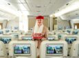 An Emirates crew member is holding one of the new amenity kits while standing in the aircraft cabin.