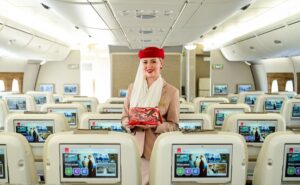 An Emirates crew member is holding one of the new amenity kits while standing in the aircraft cabin.