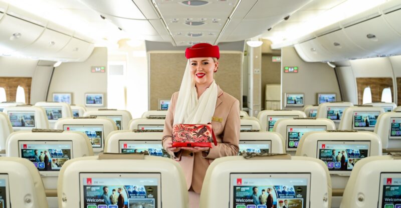 An Emirates crew member is holding one of the new amenity kits while standing in the aircraft cabin.