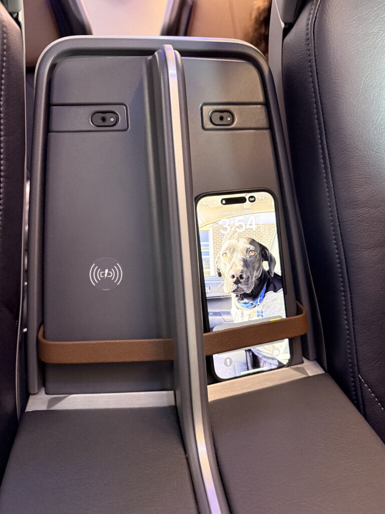 A passenger's phone sits in the wireless charging area of the Premium Economy class seat.