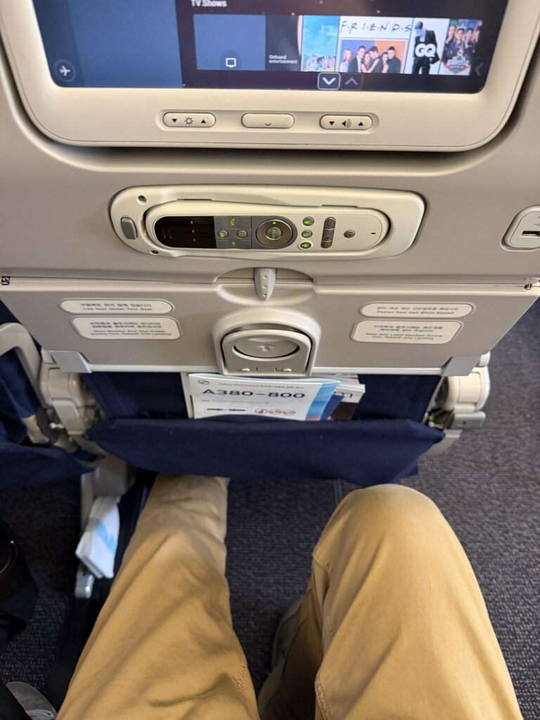 A passenger's knees are seen a distance away from the seat in front of them.