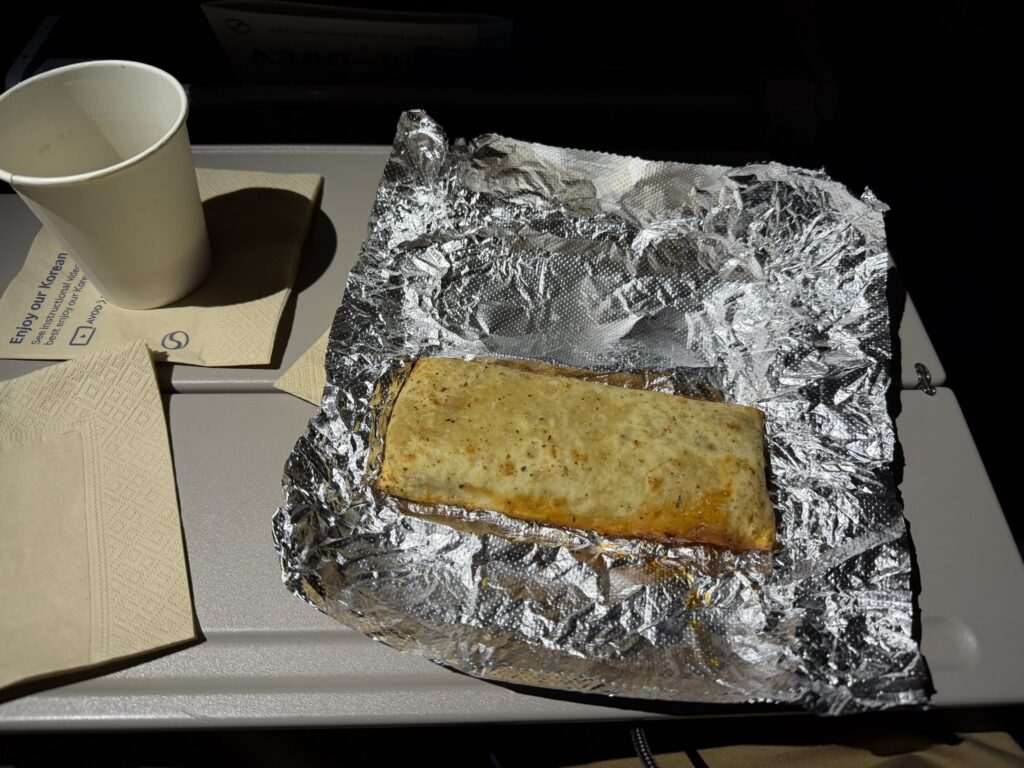 A hot pocket is sitting open and ready to eat on the aircraft tray table.
