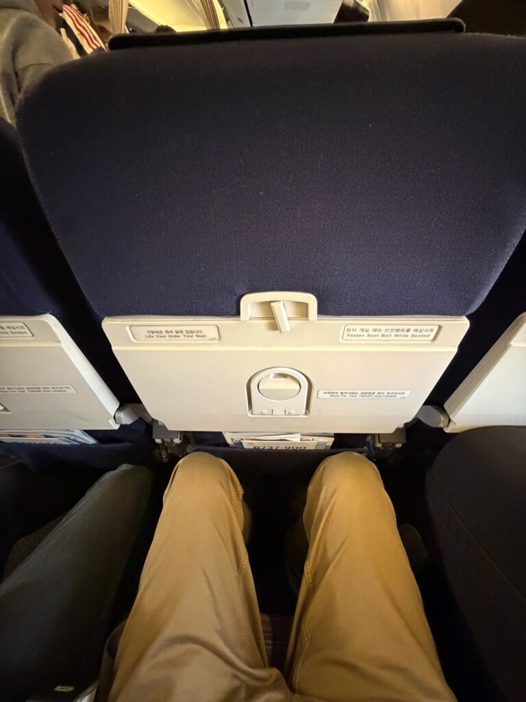 A man's knees are shown a decent distance away from the seat in front of him.