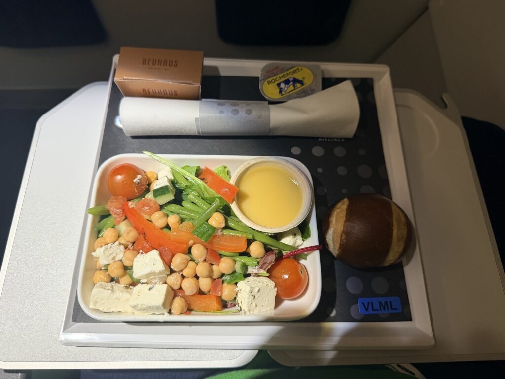 The passenger displays his meal consisting of a chickpea salad and pretzel bun.