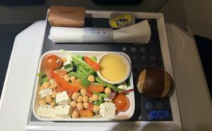 The passenger displays his meal consisting of a chickpea salad and pretzel bun.