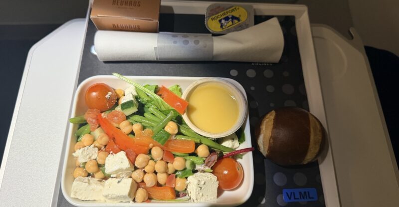 The passenger displays his meal consisting of a chickpea salad and pretzel bun.