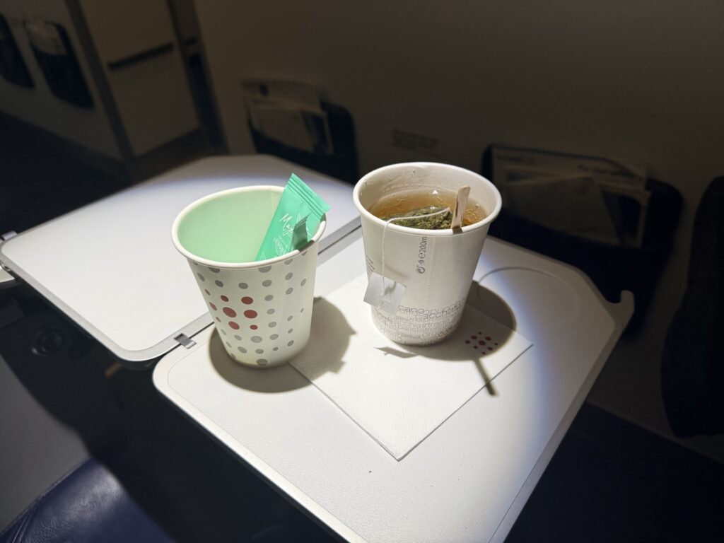 A cup of green tea is sitting on the aircraft tray table. 