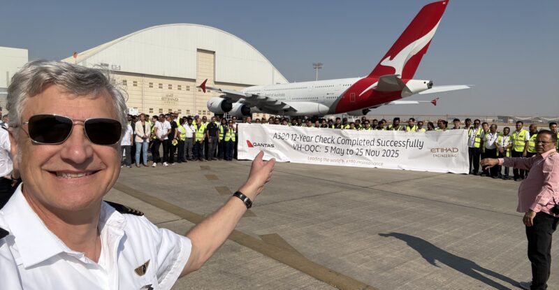 The Qantas A380 is at a hangar. Various members of the Qantas team are holding a banner and posing for a photo in celebration.