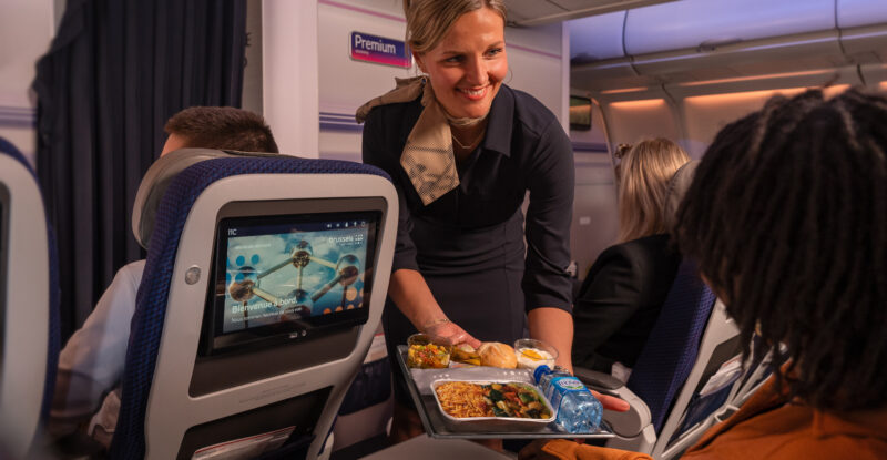A Brussels Airlines crew member is handing a meal to a passenger.