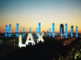 LAX Pylons light up blue behind the LAX sign during sunrise.