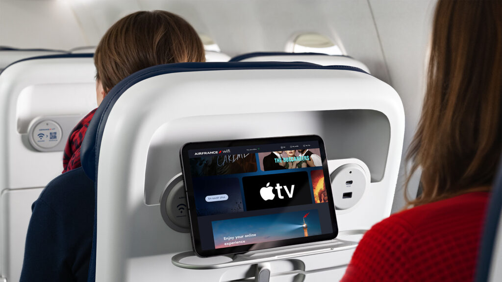 A mobile device is held in a seatback PED holder. The device is displaying Apple TV.