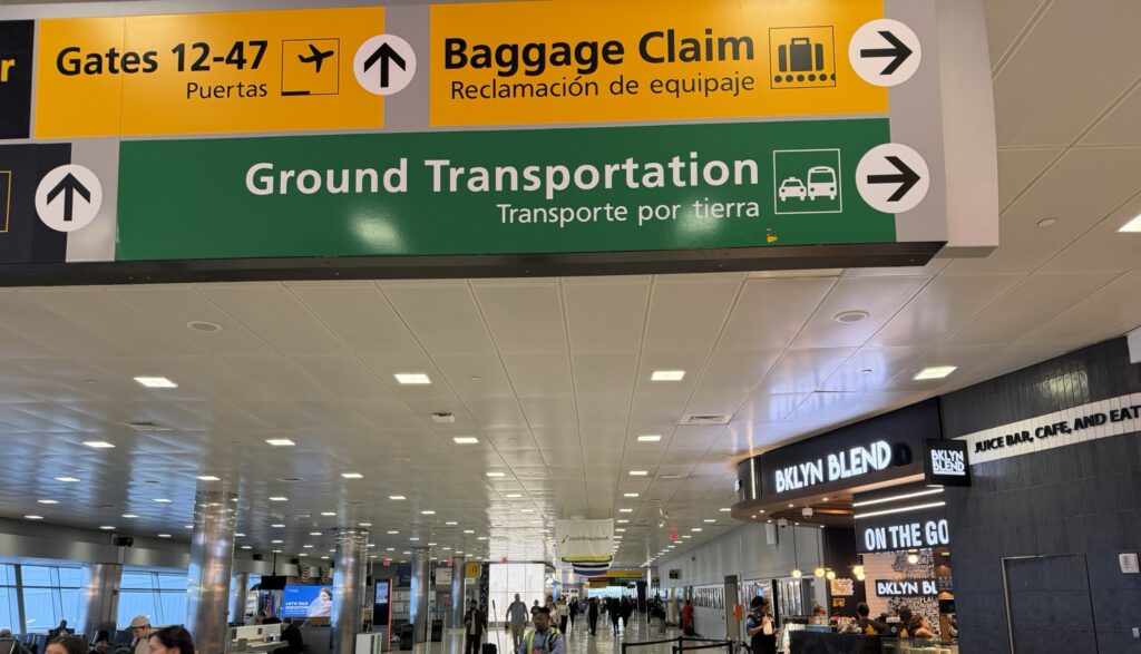 Directional airport signs at JFK Terminal 8 are near a juice bar.