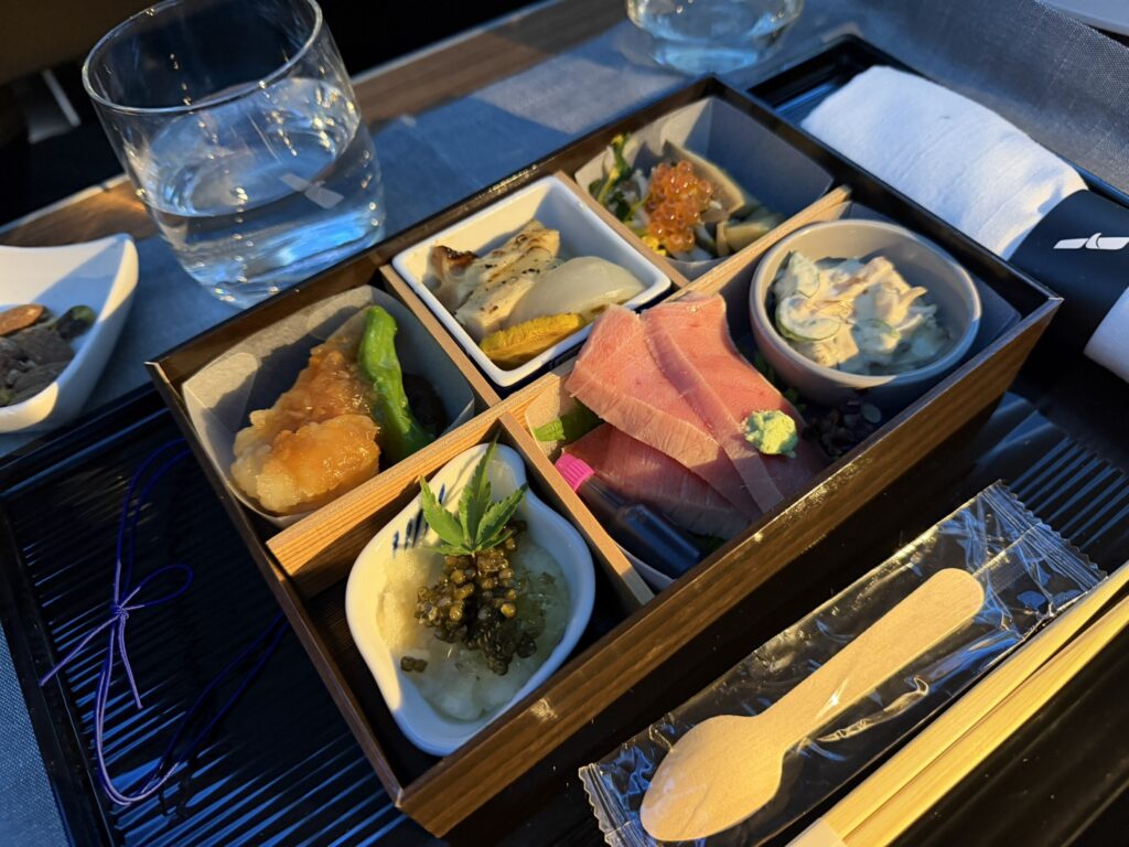 A bento box is elegantly displayed on the passenger's tray table.