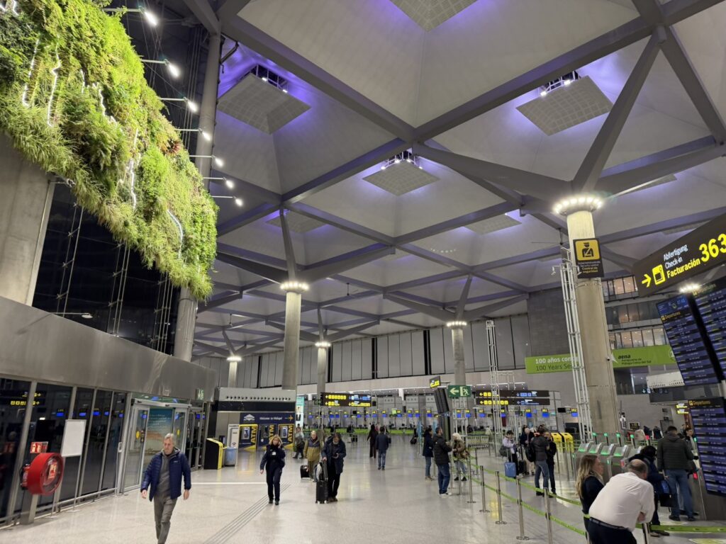 A clam scene at Malaga Airport with purple mood lights overhead and greenery on the wall.