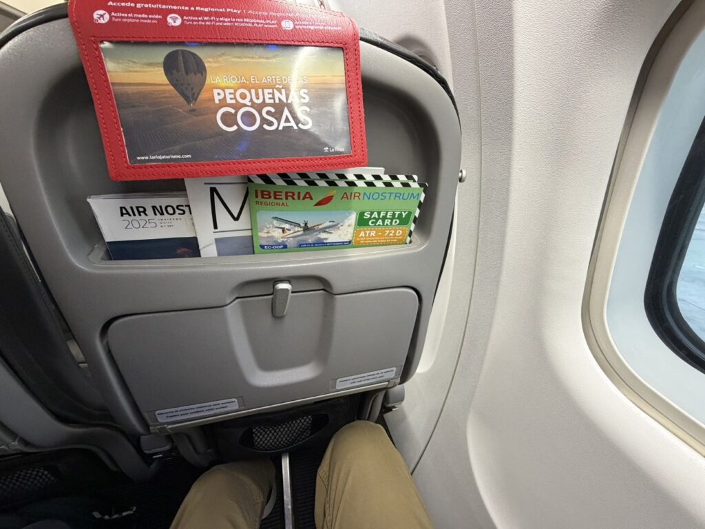 Various flyers and safety cards are tucked into the aircraft literature pocket and the headrest cover doubles as an advertisement pocked for the seat behind it. 
