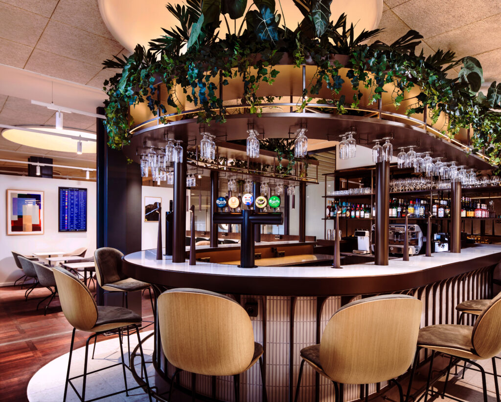 A large bar in rich wood tones and accents accented by greenery in the Aspire Executive Lounge by Zebra.