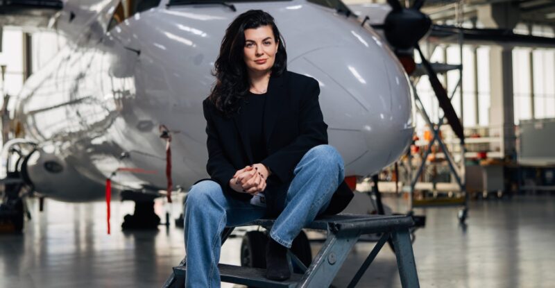 Anastasija Visnakova of Deutsche Aircraft is sitting in front of an aircraft.