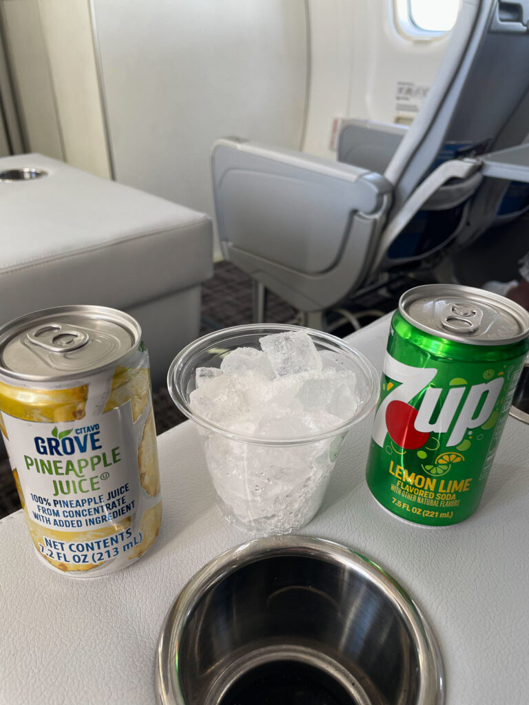 Two drinks and a cup of ice sit on the aircraft table.