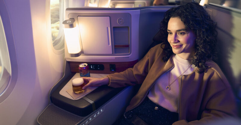 Alaska Airlines International Business Class seat is occupied by a passenger enjoying a drink.
