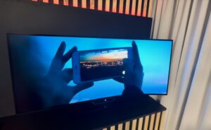 Ultra-wide Astrova Curve screen is pictured. Content is running on the screen, showing a person using their smart phone to capture the image of a sunset. The screen is highly immersive.