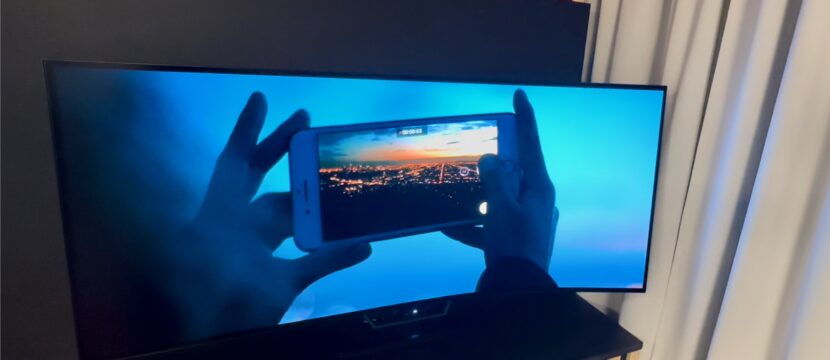 Ultra-wide Astrova Curve screen is pictured. Content is running on the screen, showing a person using their smart phone to capture the image of a sunset. The screen is highly immersive.
